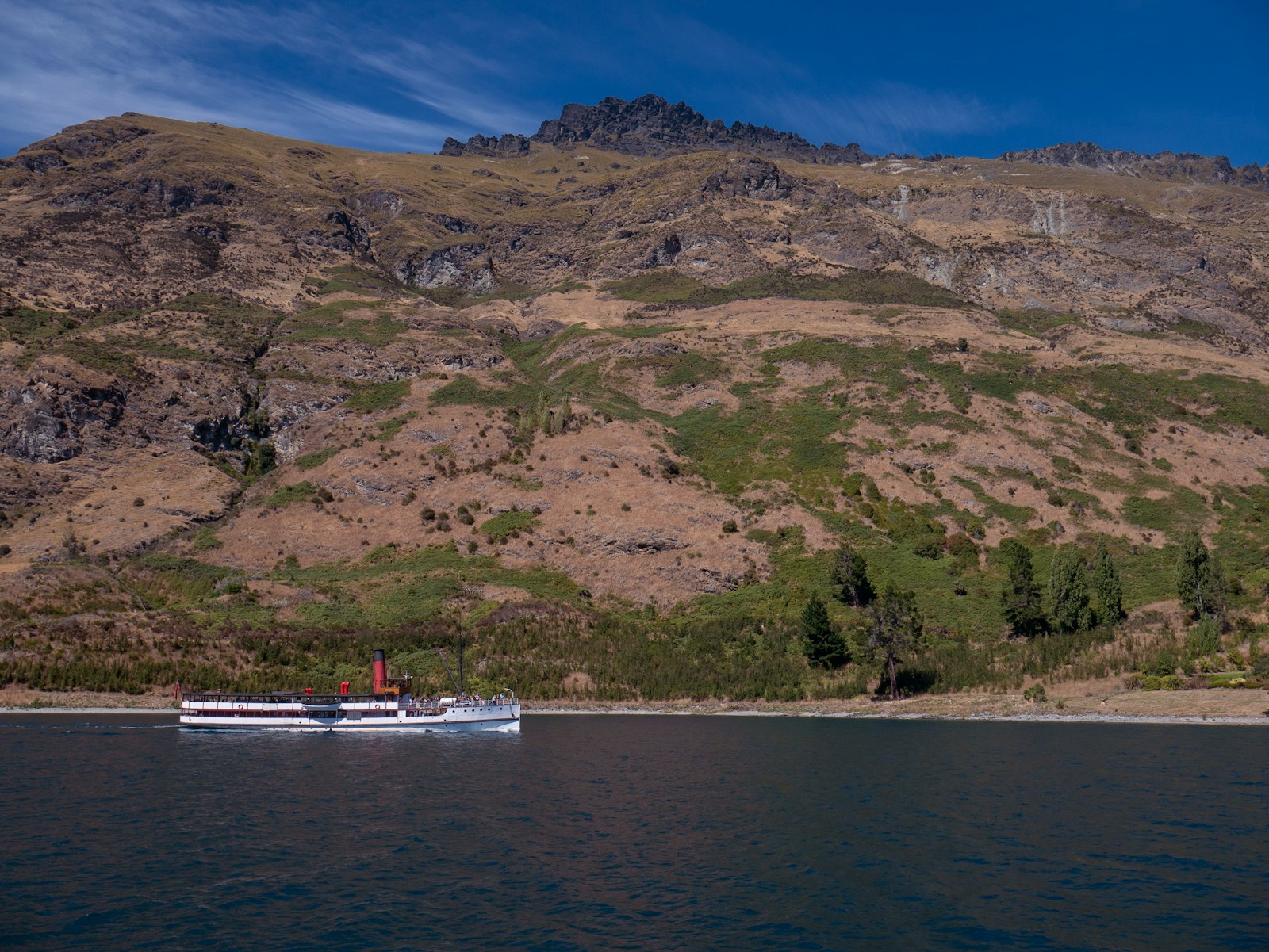 Boat cruising Lake Wakatipu in summer with mountains in the background